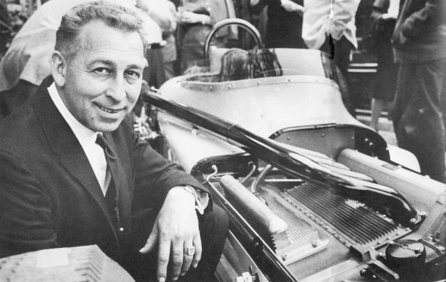 Black and white photograph of George Salih kneeling next to a race car.