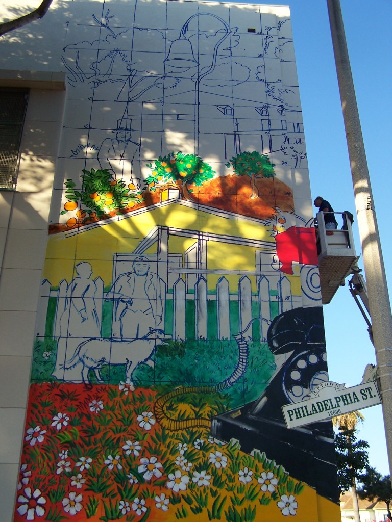 Day 8: Photograph of the section of the mural facing Philadelphia St. The bottom section of the Bailey House is mostly complete and the top section, Pio Pico's mansion is just outlined in blue paint.