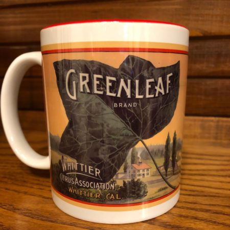 Photograph of coffee mug with Greenleaf Brand graphic on the front. Mug has white background and red color on the interior of the mug.