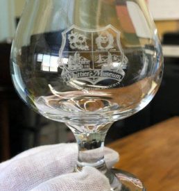 Photograph of a brandy glass with the Whittier Historical Society coat of arms etched onto the glass.