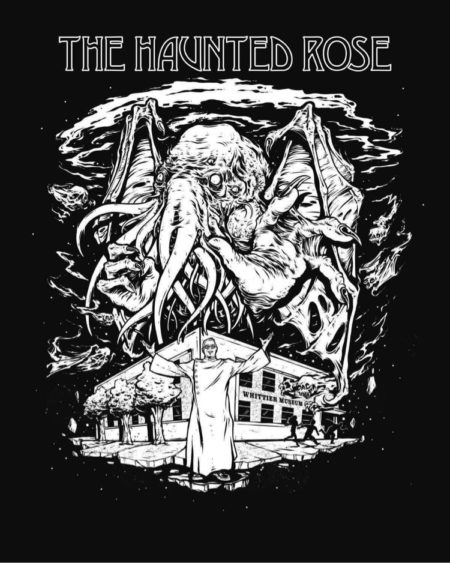 Photograph of the 2021 Haunted Rose graphic. T-shirt is short sleeved, black with a white graphic which shows a monster above the Whittier Museum. The Whittier Historical Society coat of arms is on the sleeve